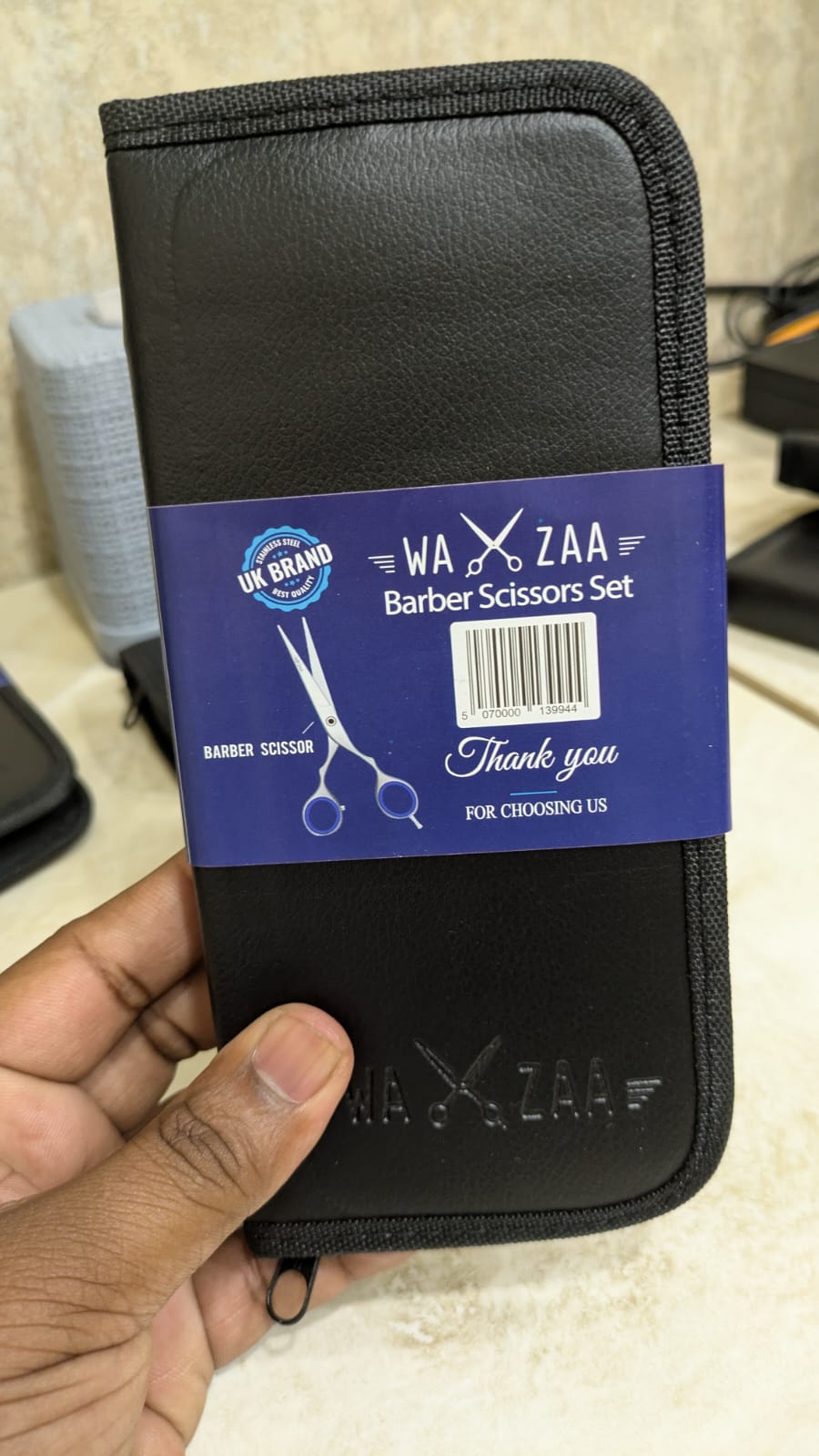 Black case with a blue label featuring 'WAZAA' branding, held by a hand.