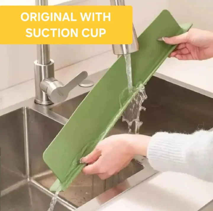 Green cutting board with suction cup being rinsed under running water in a kitchen sink.