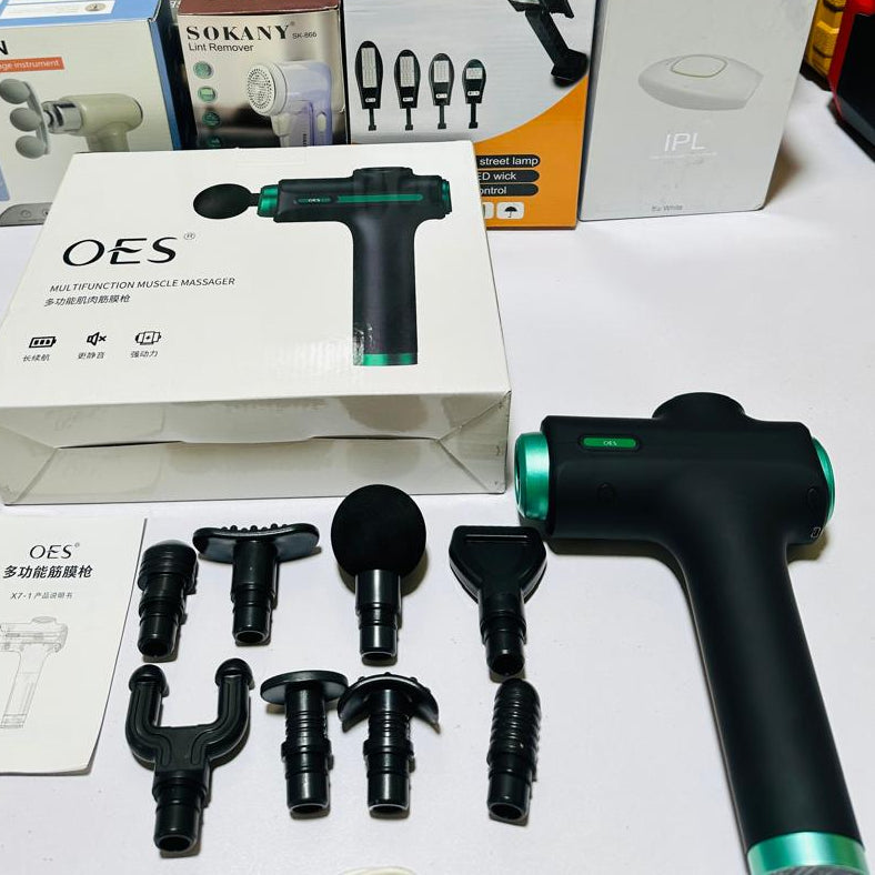 Massage gun with attachments on a white surface, surrounded by packaging boxes.