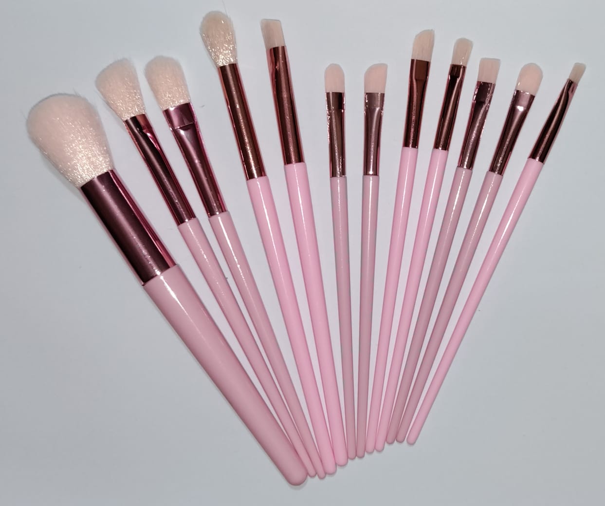 Set of makeup brushes with pink handles and brown ferrules on a light gray background