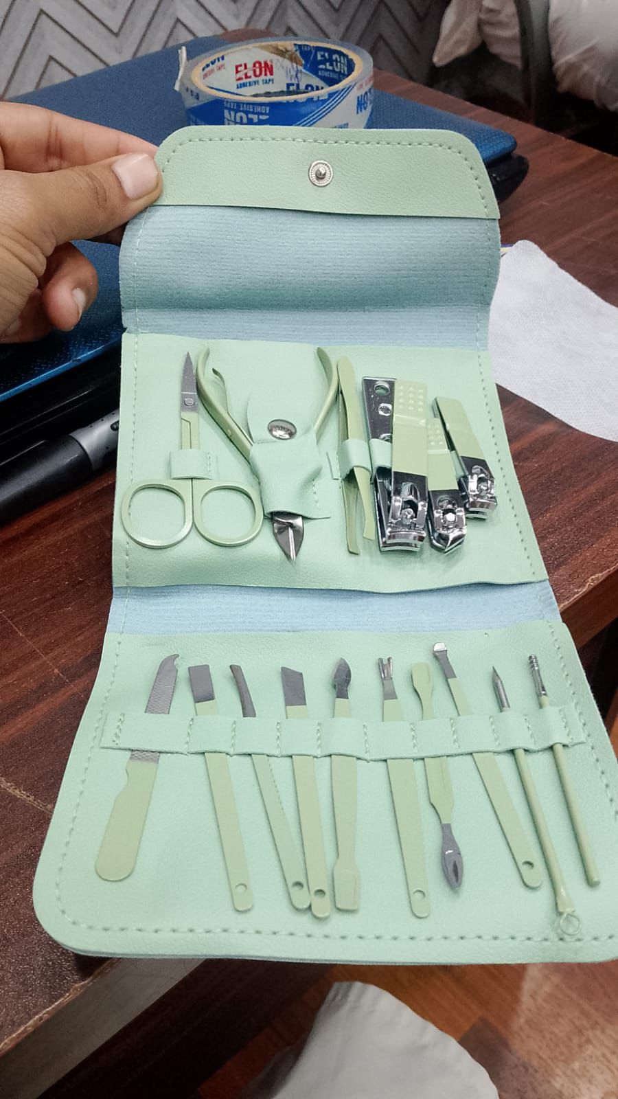 Set of manicure tools in a light green case on a wooden surface.