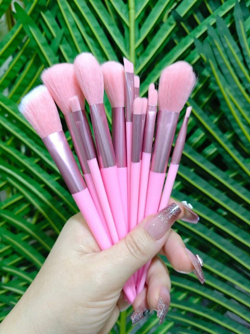 Set of pink makeup brushes held in a hand against a green leafy background