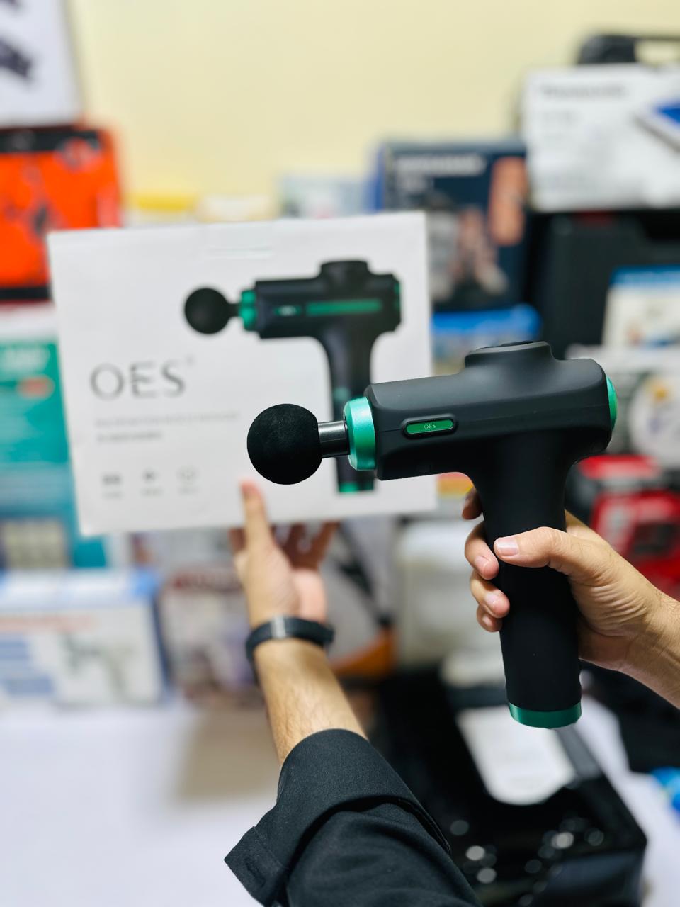 Person holding a massage gun with a blurred background of products and packaging